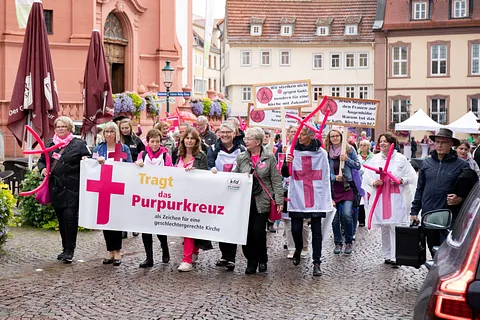 Viele Frauen tragen ein Banner vor sich mit purpurfarbenen Kreuz und Text "Tragt das Purpurkreuz"