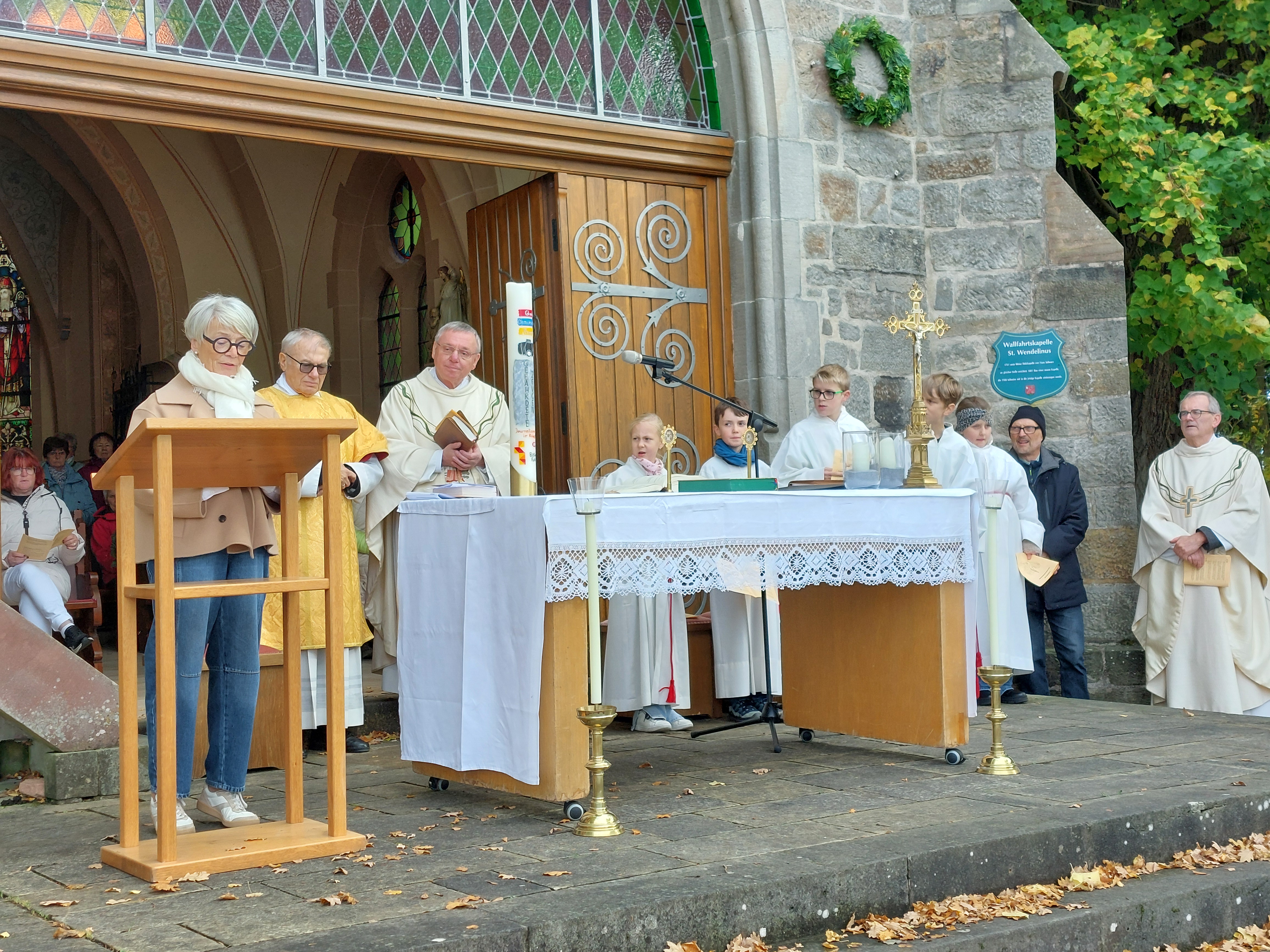 Frau am Vorlesepult, hinter dem Altar Priester und Messdiener