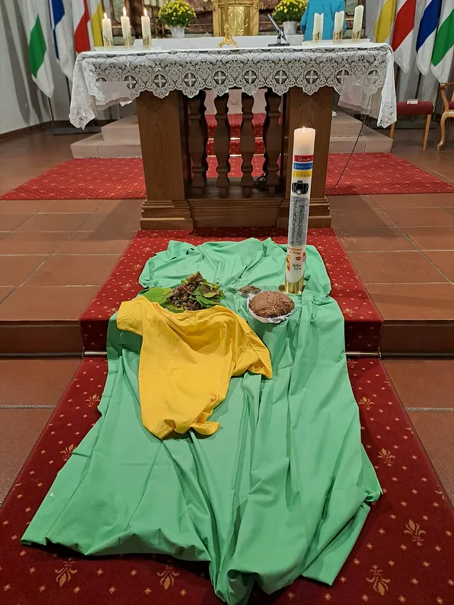 Auf dem grünen Tuch vor dem Altar liegt ein Brot und Trauben und ein gelbes Tuch. Die große Kerze steht im Mittelpunkt.