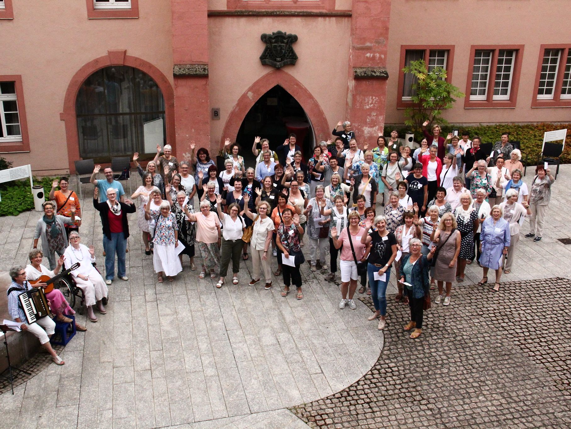 Eine Gruppe von Frauen stehen im Innenhof und winken nach oben.