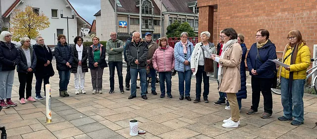 Auf dem gepfalsterten Platz stehen Frauen und Männer im Halbkreis um die Kerze, eine liest von einem Blatt vor.