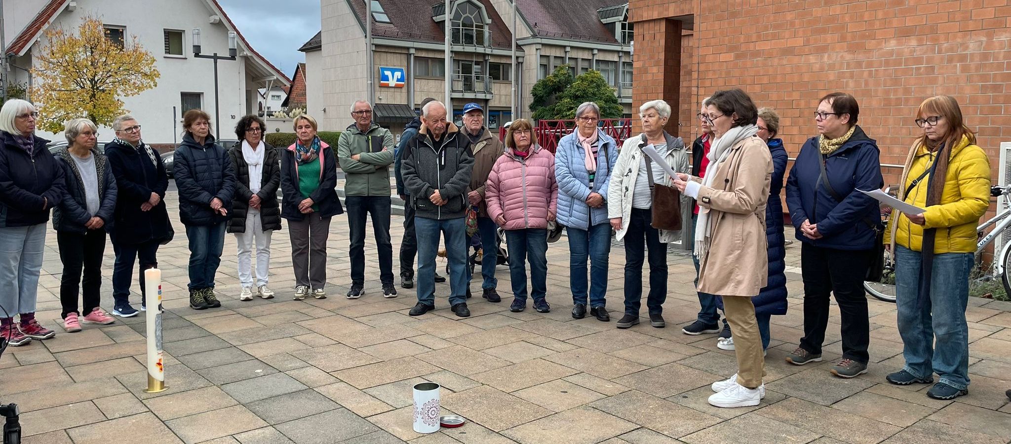 Auf dem gepfalsterten Platz stehen Frauen und Männer im Halbkreis um die Kerze, eine liest von einem Blatt vor.