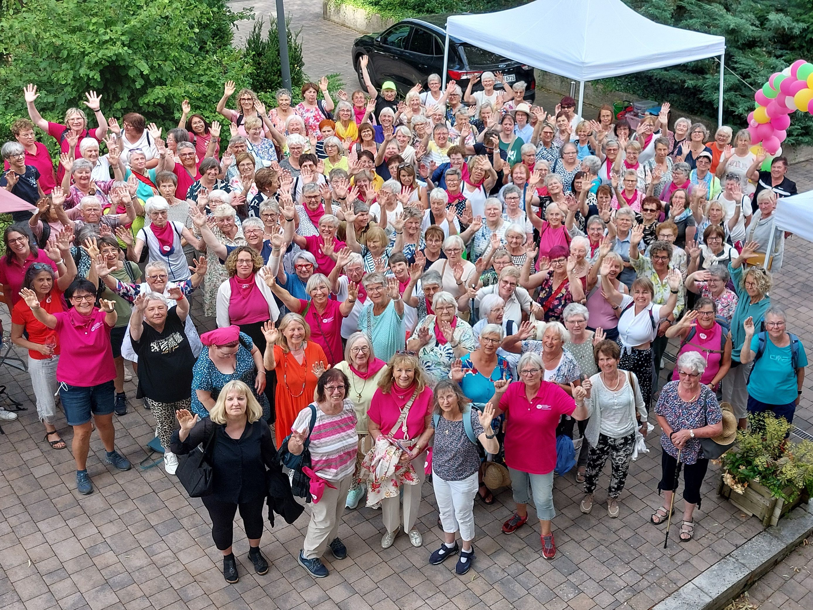 Gruppe von bunt gekleideten Frauen schauen nach oben und winken.