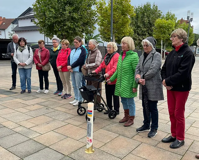 Auf dem gepfalsterten Platz stehen Frauen und ein Mann hinter der entzündeten Kerze.