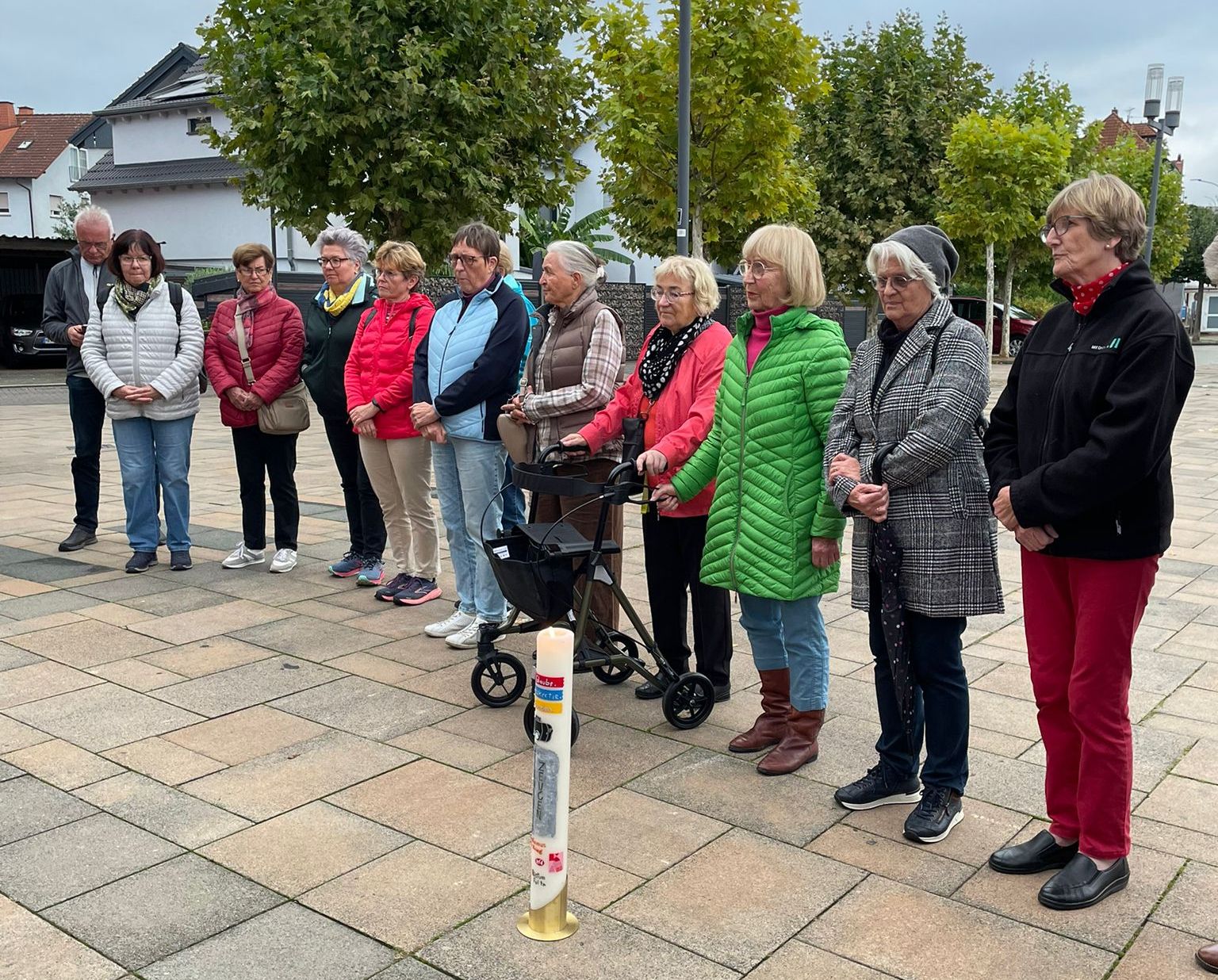 Auf dem gepfalsterten Platz stehen Frauen und ein Mann hinter der entzündeten Kerze.